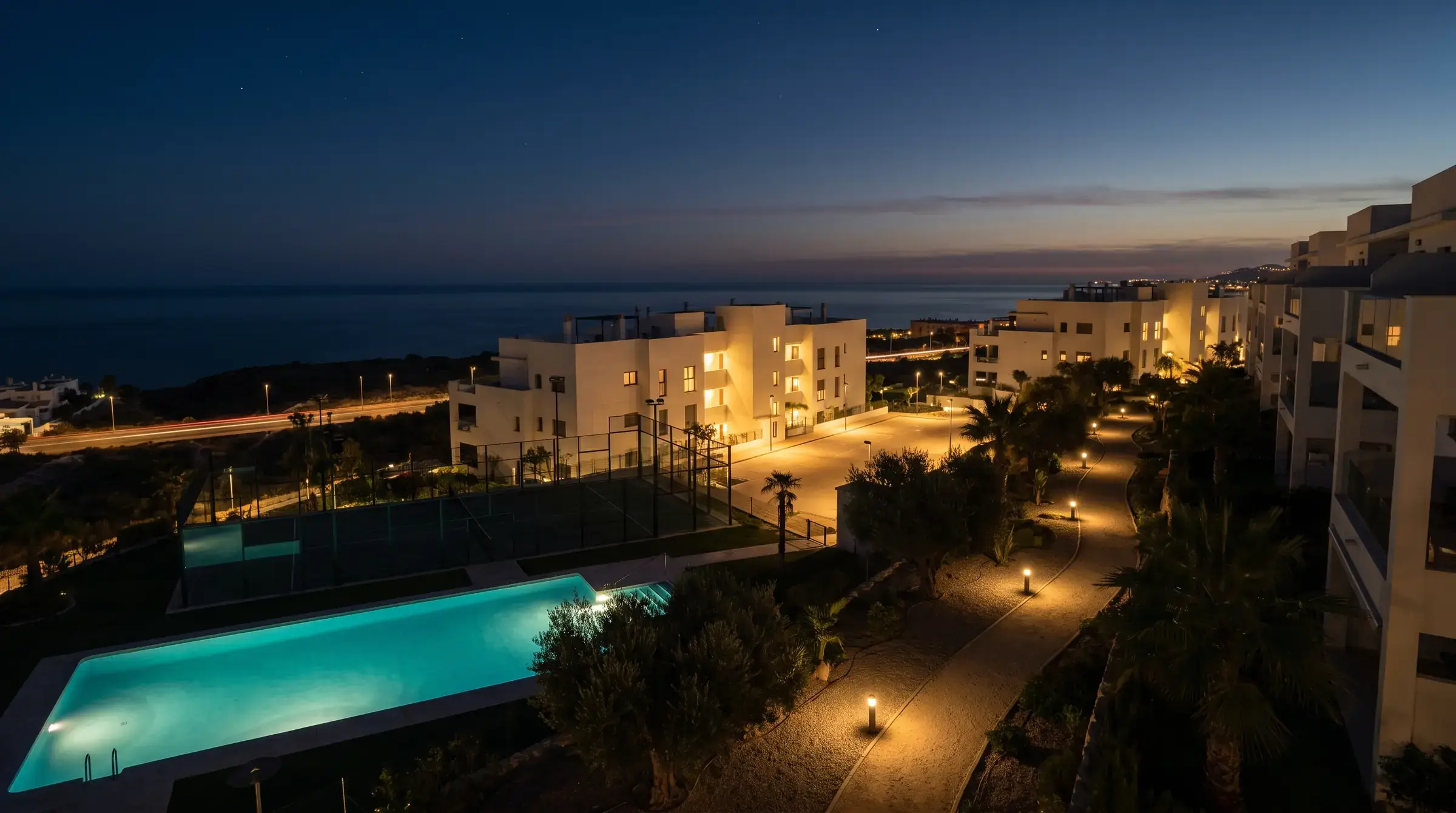 Urbanización mediterránea de noche con la piscina iluminada y las ventanas encendidas
